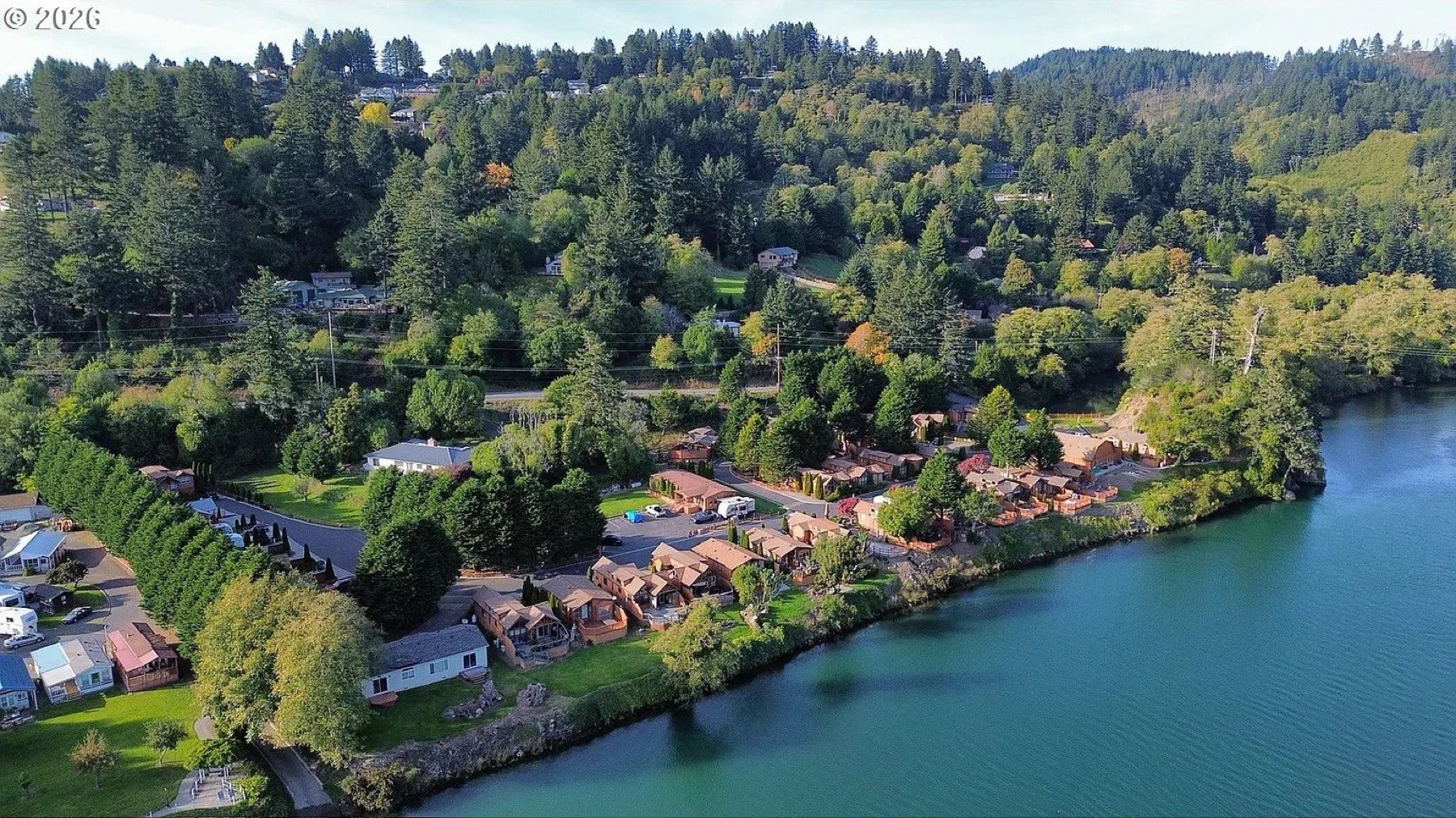 Aerial view of Chetco River Resort homes along the Chetco River with forested hills behind
