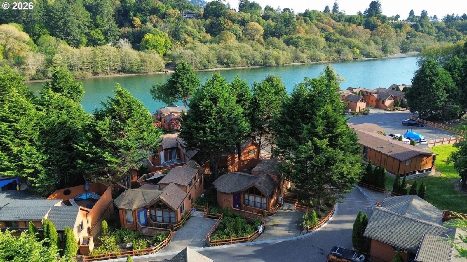 Cedar homes beneath tall trees with the Chetco River beyond at Chetco River Resort